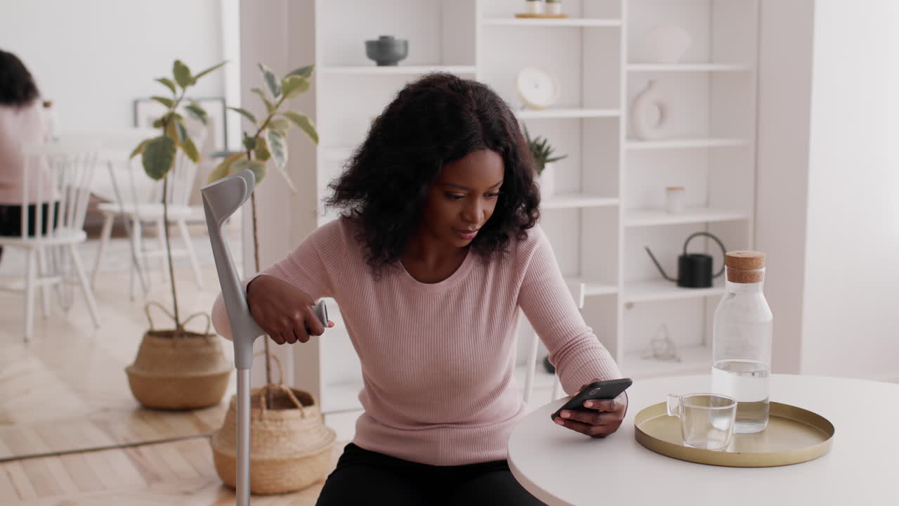 Woman using a phone while resting in a cafe with a crutch