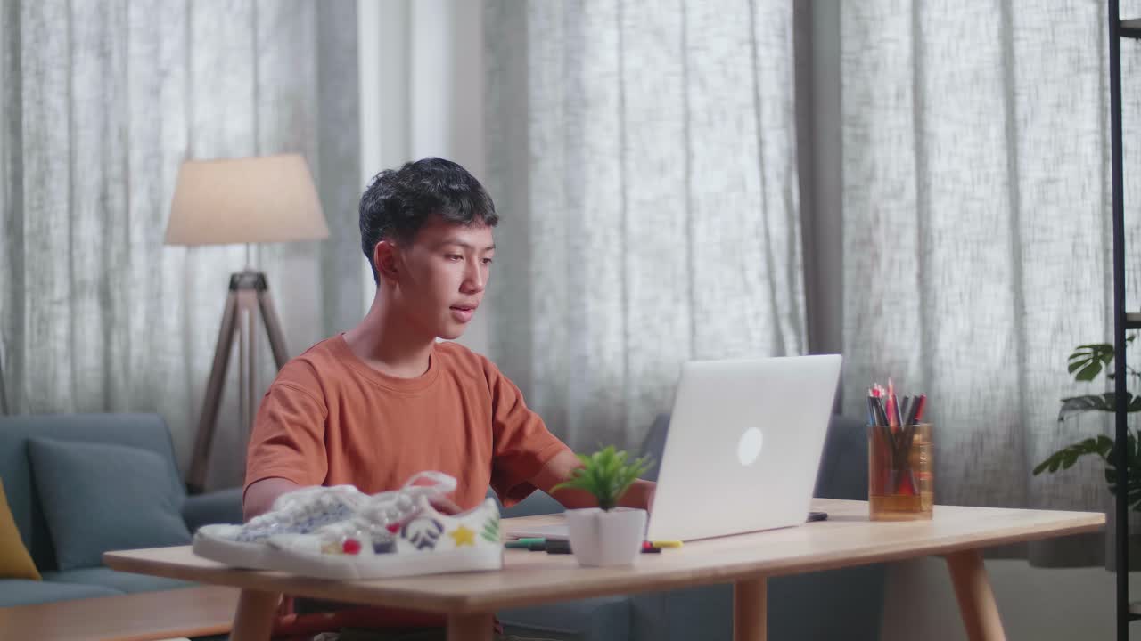 아시안 소년 신발 디자이너가 집에서 노트북으로 디자인하고 있습니다.