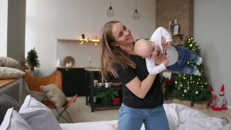 vamos a volar alegre mujer joven hermosa sosteniendo a la niña en sus manos y mirándola con amor mientras está sentada en el sofá en casa