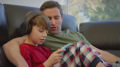 padre con su hijo usando auriculares inalámbricos jugando a un juego de computadora en un dispositivo portátil - filmado en cámara lenta