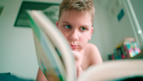 the footage in high definition of a kid lying and reading a book, turning pages