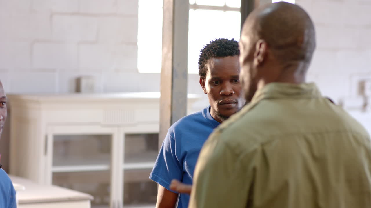 Pointing African American male colleagues examining workshop area, with earmuffs and cabinets