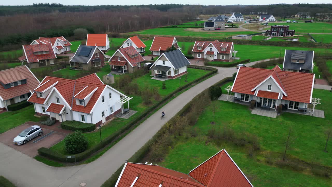 Droneudsigt over afsidesliggende landsby med huse og haver og et barn, der cykler på gaden