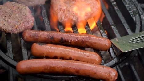 outdoor grill closeup as seasoned beef hamburger patties and hot dogs are turned over flames with smoke