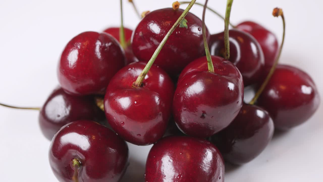 Buah ceri merah segar berair berputar di latar belakang putih. Tampilan samping
