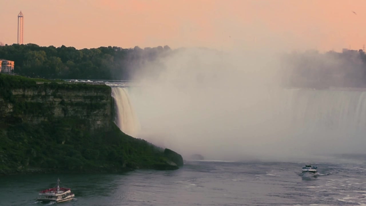 Huczące wodospady Niagary ujęte od strony kanadyjskiej o zachodzie słońca. Łodzie „Maid of the Mist” płyną w pobliżu wodospadów.