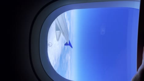 close up of passenger man hand opening airplane window blind from which airplane wing and clouds can be seen