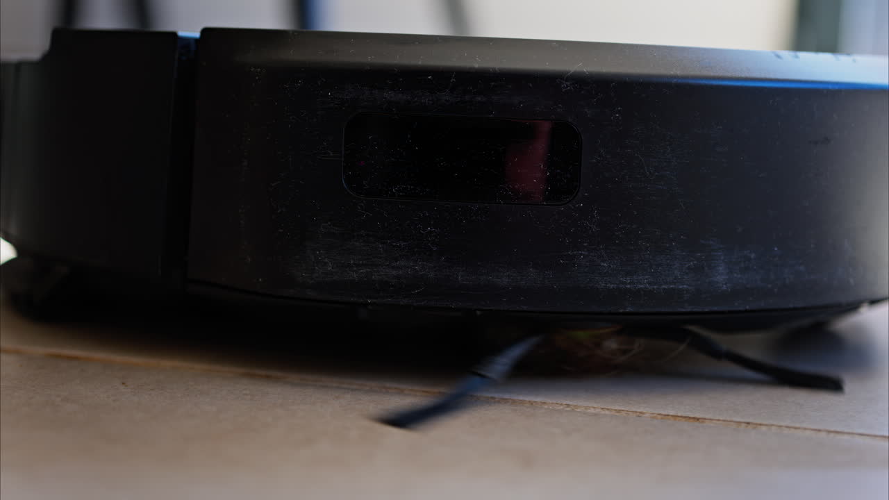Close up of a small, black robot vacuum cleaning the house