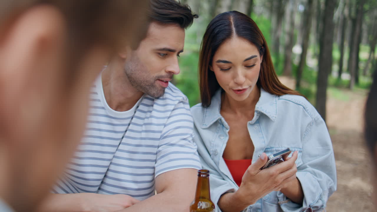 Picnic couple looking cellphone sitting park with friends closeup. Happy people