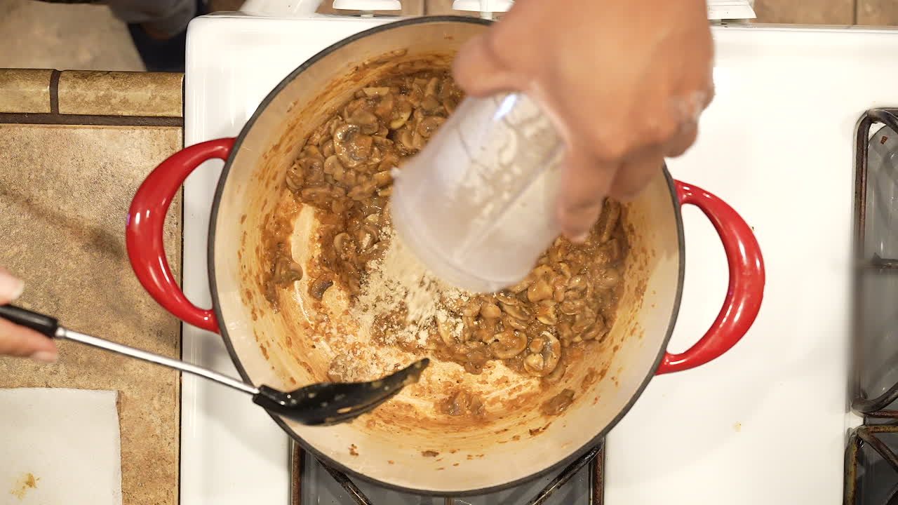 Aggiunta di amido di mais e brodo a funghi saltati in una pentola sul fornello per addensare la zuppa - vista dall'alto SERIE RISO SELVATICO