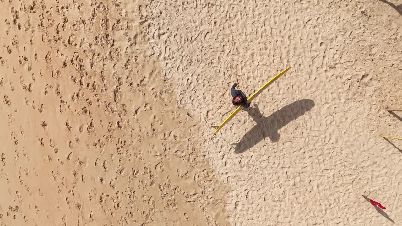 Aerial view of a person with surfboard on a sandy beach