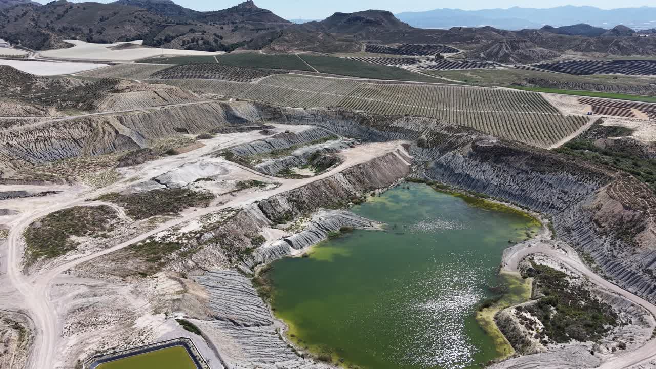 An orbiting drone shot of a massive open-pit mine and water depuration plant, showing the scale of excavation against the arid Spanish landscape
