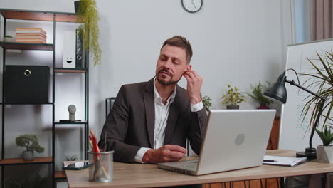 Businessman-working-on-laptop-at-office-wearing-earphones-listening-favorite-energetic-disco-music