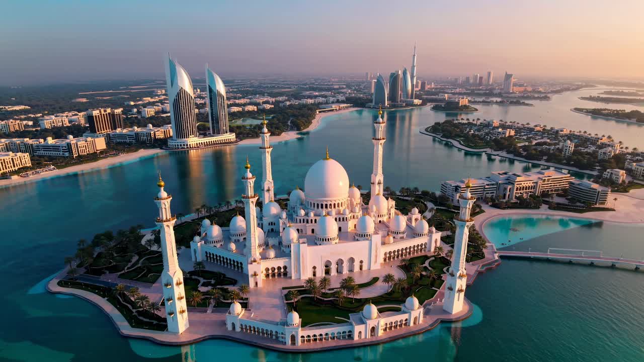 Aerial view of a grand mosque surrounded by water and cityscape at sunset, capturing a serene