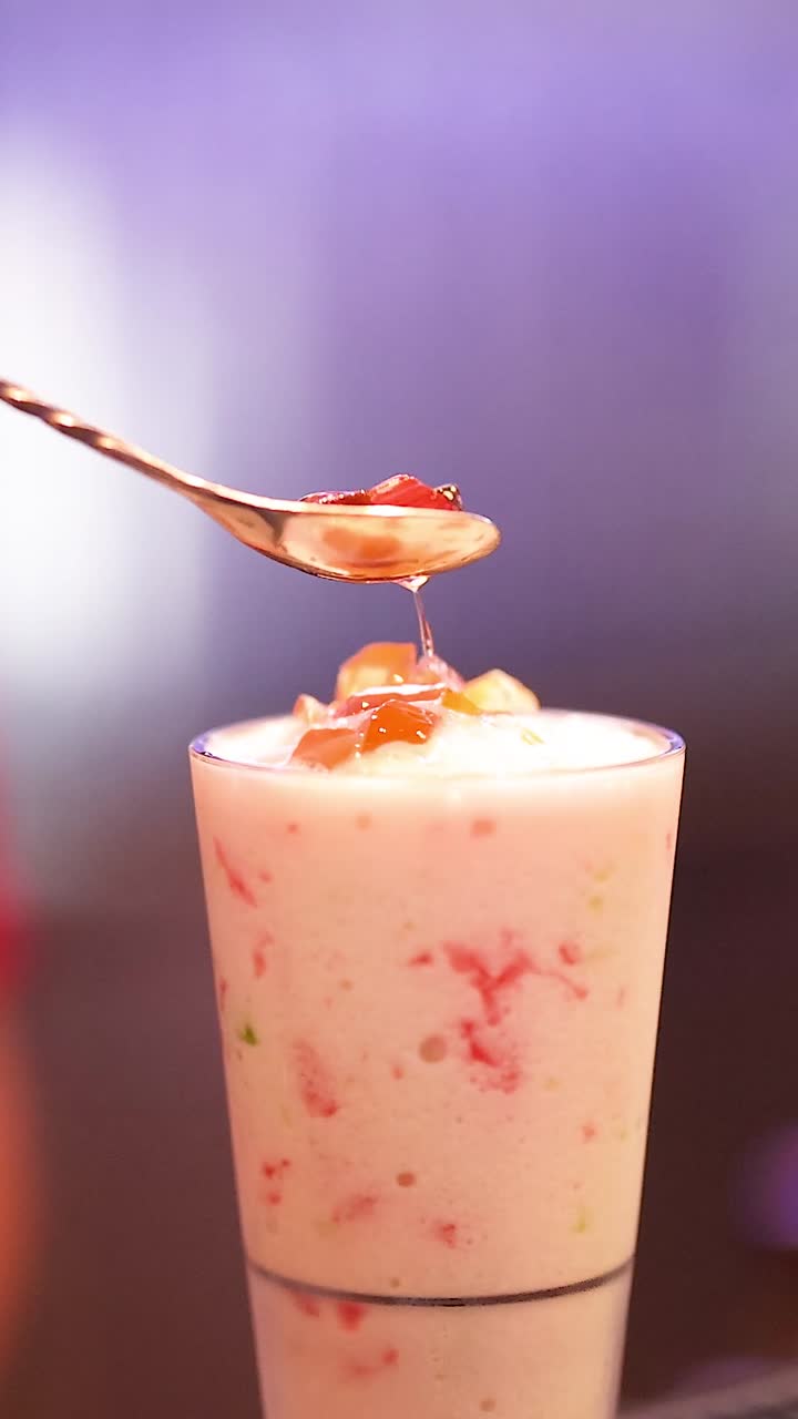 Metallilusikka asettaa varovasti hedelmäpäällisiä paksun, vaaleanpunaisen smoothien päälle lasissa.