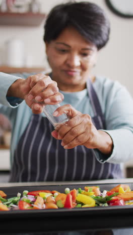video vertical de una mujer biracial senior cocinando en la cocina