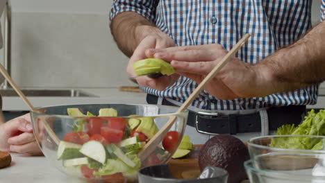 close up of man hands adding avocado slices in a glass bowl to prepare an healthy and tasty salad