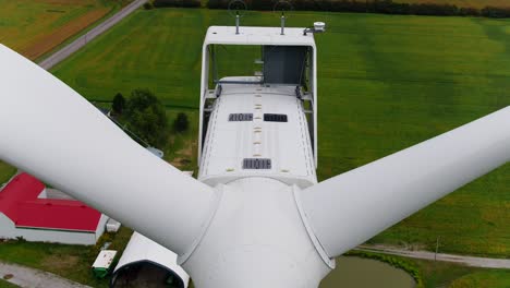 Turbina-Eólica-Cerca-De-Un-Dron-Ascendiendo-Sobre-Las-Palas-De-La-Hélice-Con-Una-Vista-De-Arriba-Hacia-Abajo,-Tierras-De-Cultivo-En-El-Fondo