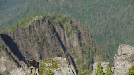 photographer takes shaka selfie with phone on mountain ridge with epic view, tim durkan wide tracking helicopter counterclockwise orbit slow motion