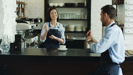 joyful young waitress and waiter having fun and dancing while serving coffee to the beautiful woman at the bar