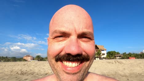 close up of caucasian male with moustache smiling in front of camera at beach