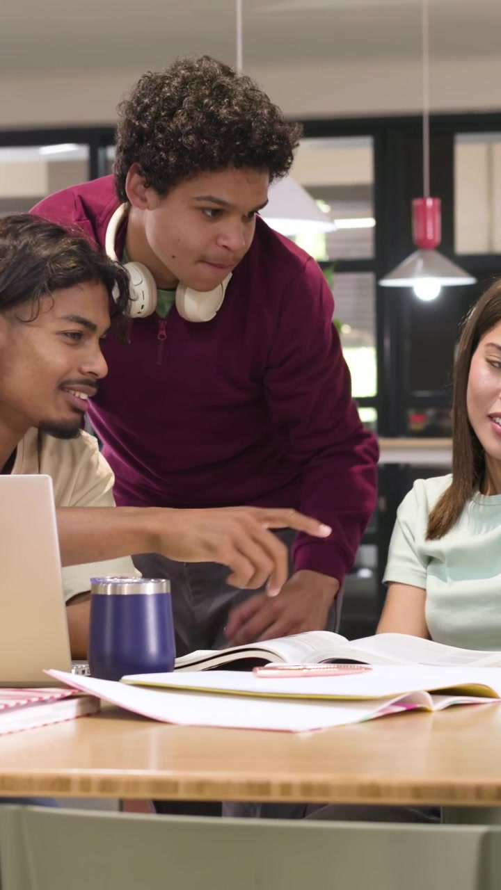 Vertical video: Walking up, man in maroon pullover pointing and collaborating on textbooks at table