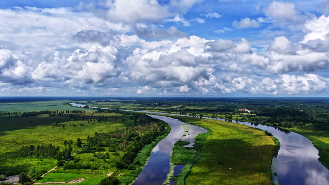 A beautiful aerial trucking shot moves sideways over the winding Lielupe River near Jelgava, Latvia, showing the lush green landscape and cloud reflections on the water