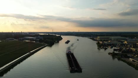 aerial static shot over beneden merwede during sunset with silhouette of barge travelling along underneath