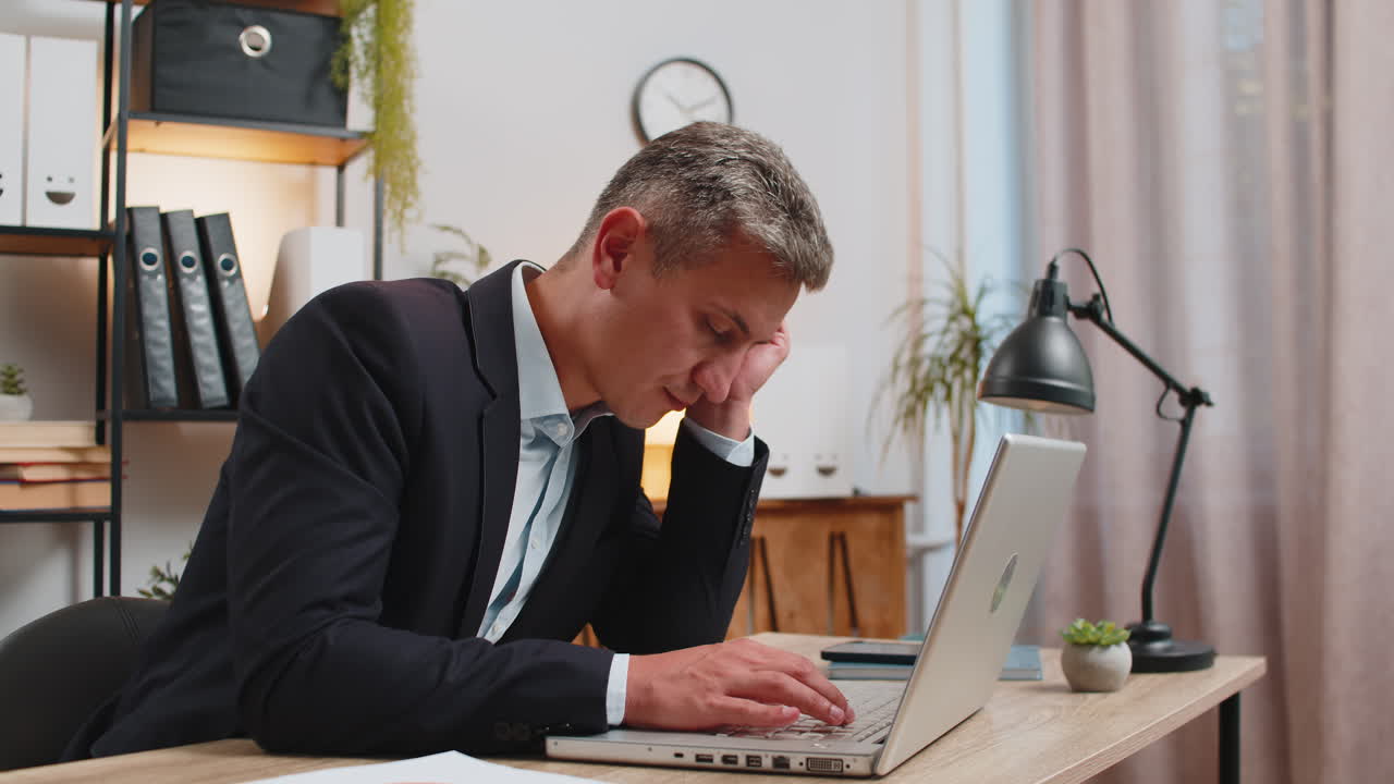 Bored caucasian young businessman sitting with laptop computer while sleeping at home office desk