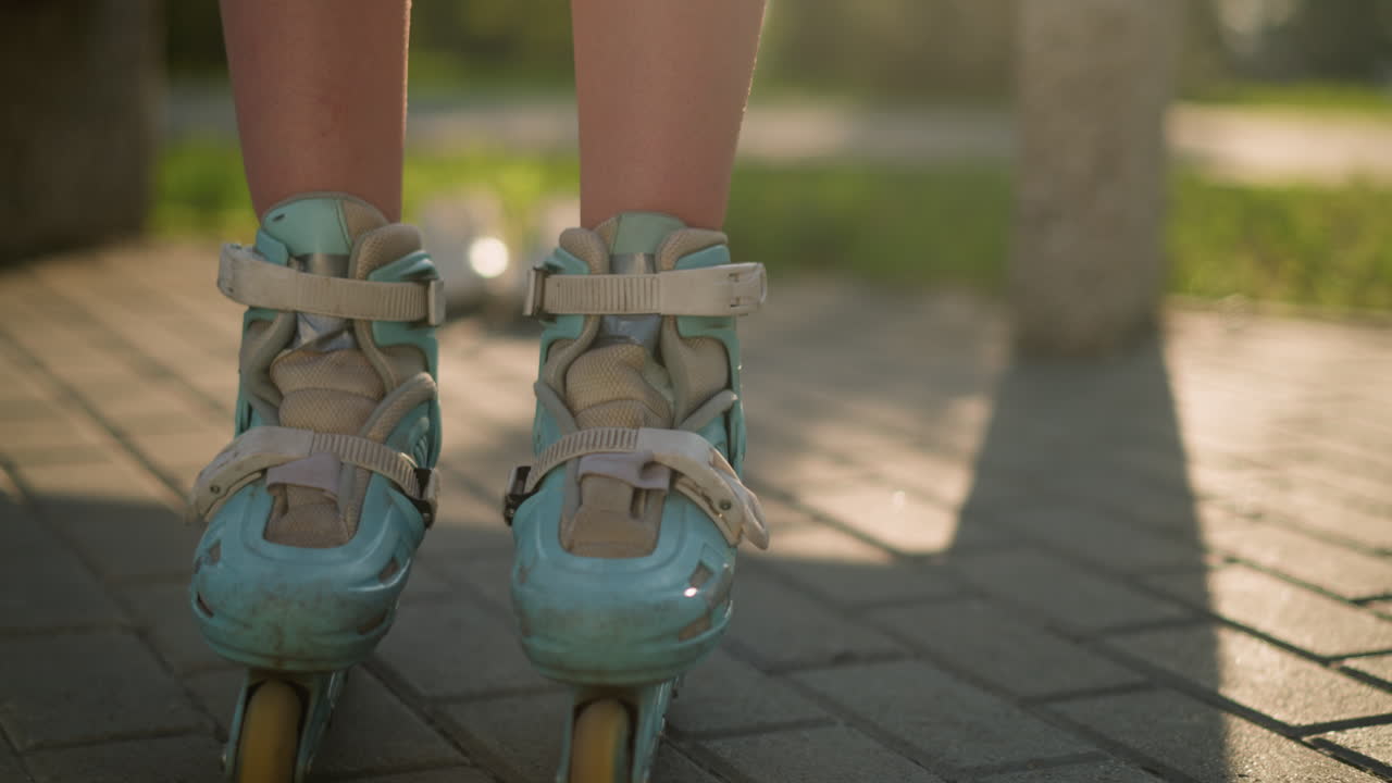 Close-up leg view of individual skating along interlocked path, moving gently under warm sunlight, casting long shadows across the ground, surrounded by greenery