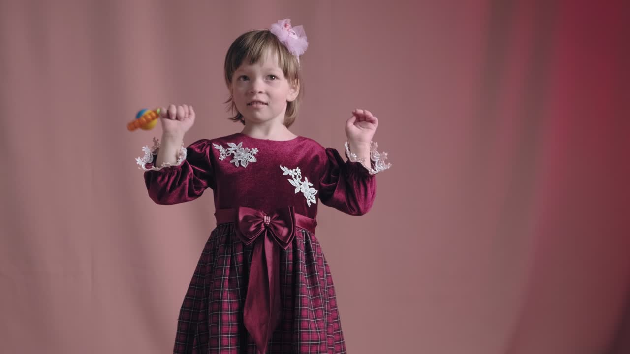 Cute little girl in an vintage burgundy dress is playing with a rattle toy