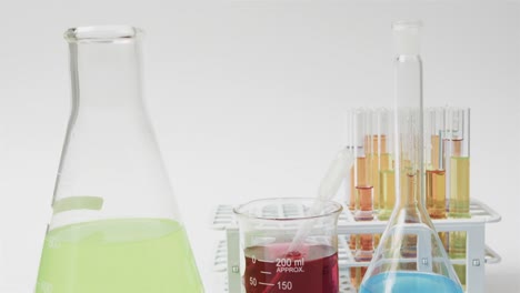 coloured liquids in flasks with test tubes in stand on white background, slow motion