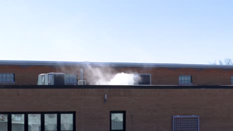 a big industrial air conditioner on a flat rooftop of a commercial building is releasing white smoke indicating how freezingly cold outside temperatures are