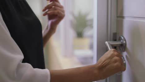 mid section of biracial businesswoman opening door with colleagues in background in modern office