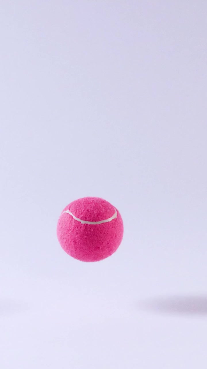 Bola tenis merah muda cerah memantul berulang kali dengan latar belakang putih bersih dalam format vertikal.