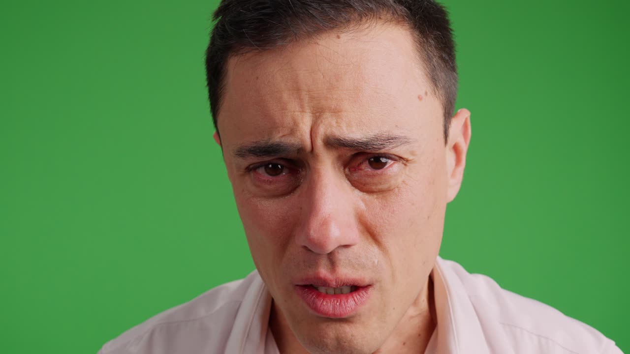 Sad man on green screen background struggling not to cry