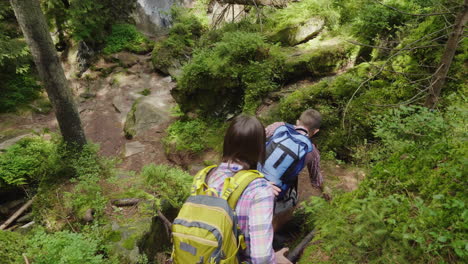 a man helps a woman to climb a steep path trekking in the forest hiking and active lifestyle