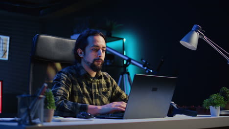 Freelancer-in-neon-lit-home-office-sitting-at-desk-and-typing-on-laptop-keyboard