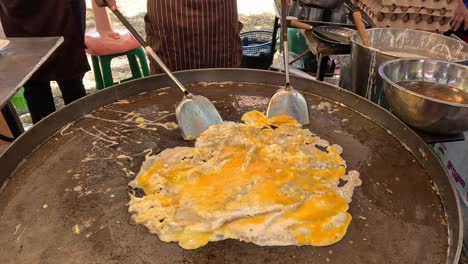 scrambled eggs being prepared on an outdoor griddle.