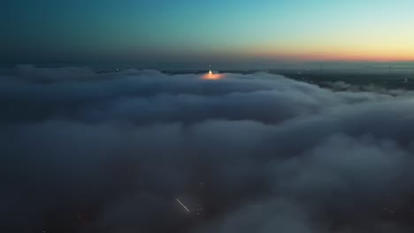 aerial flight over dense dark clouds in the air above city during sunrise at horizon