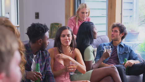 multi-cultural group of friends sitting on sofas at home together enjoying drinks and talking