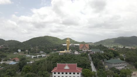 drone flying backwards from golden standing buddah statue at wat khao noi temple, hua hin