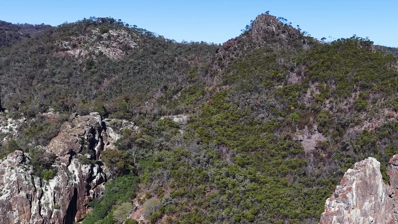 Plano estático amplo de picos vulcânicos acidentados e floresta de eucaliptos no Parque Nacional Warrumbungle, Austrália