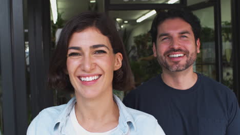 retrato de dueños masculinos y femeninos de floristas de pie en la puerta rodeados de plantas