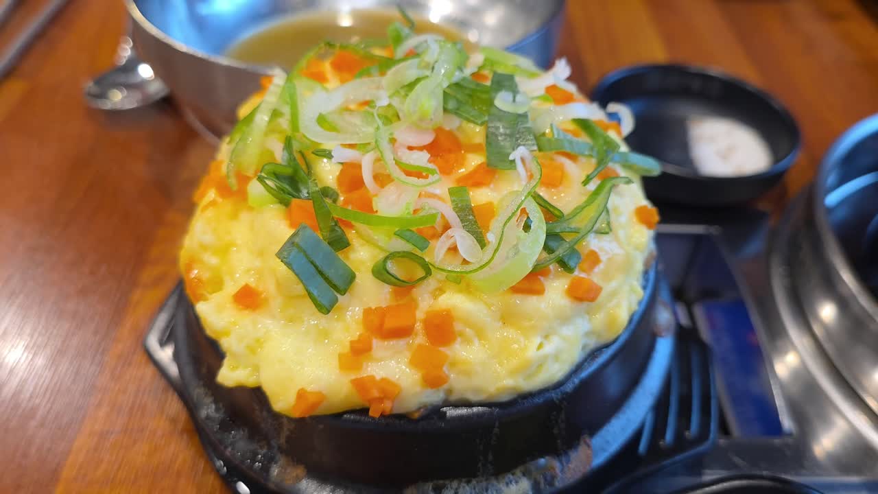 Fluffy Korean steamed egg gyeran-jjim garnished with chopped carrots and green onions in a sizzling stone bowl