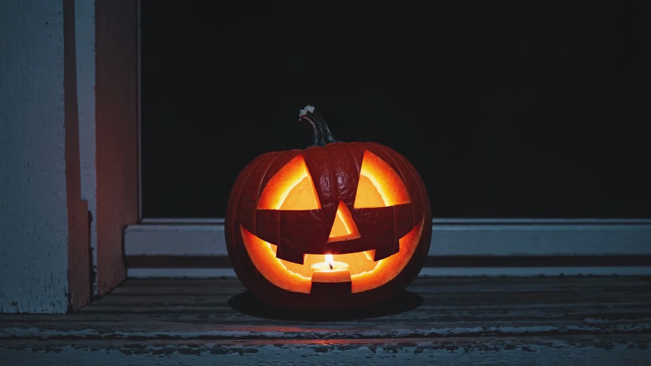 A close-up, low-angle shot of a glowing jack-o'-lantern on a wooden porch, capturing a spooky