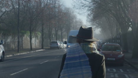 Woman-puts-on-scarf-and-walks-away-towards-incoming-traffic-in-cold-misty-morning