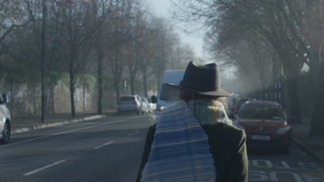 woman puts on scarf and walks away towards incoming traffic in cold misty morning