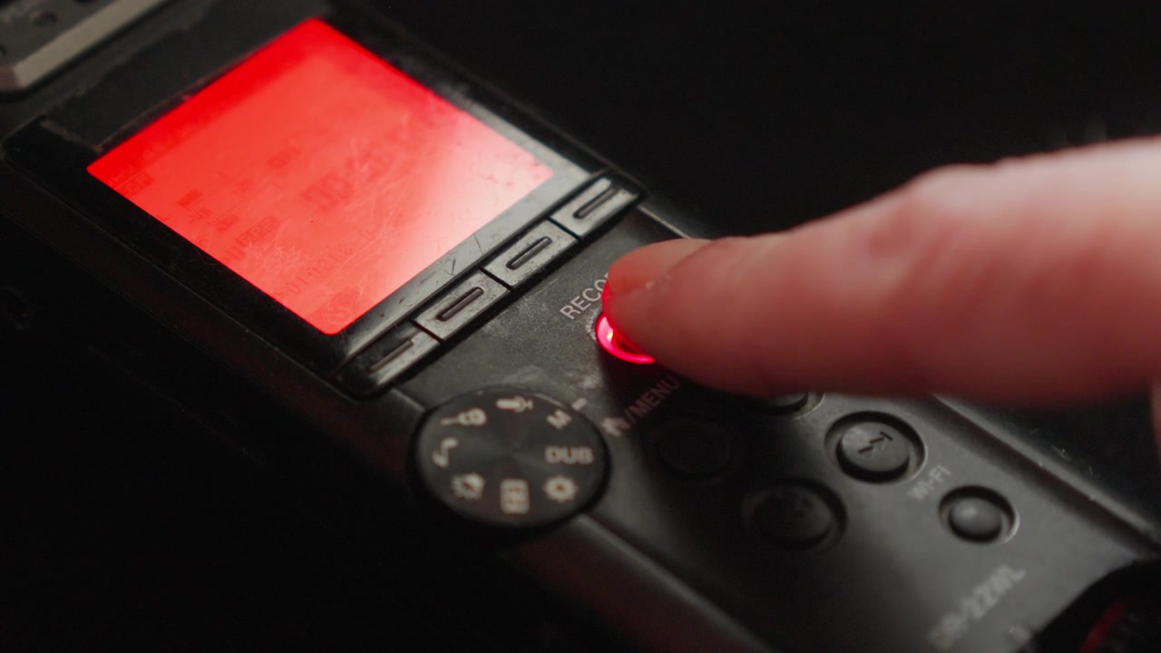 Macro primo piano di un dito che attiva la registrazione mentre un indicatore rosso si illumina, suggerendo sorveglianza, acquisizione di prove o l'inizio di una sessione di registrazione controllata.