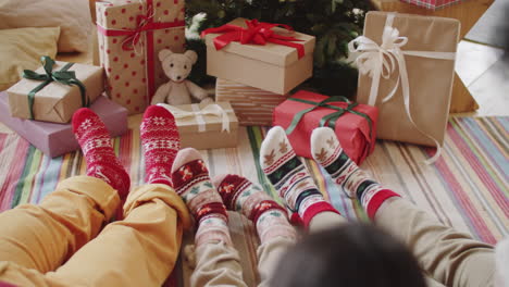 piernas de la familia en calcetines de vacaciones sentados por regalos de navidad